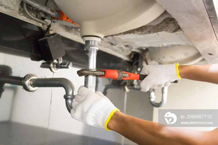 Plumber fixing white sink pipe with adjustable wrench.