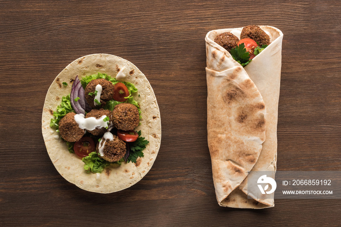 top view of falafel with vegetables and sauce wrapped and unwrapped in pita on wooden table