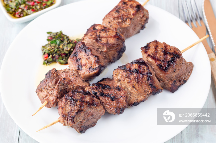 Beef meat skewers with chimichurri sauce, on white plate, horizontal