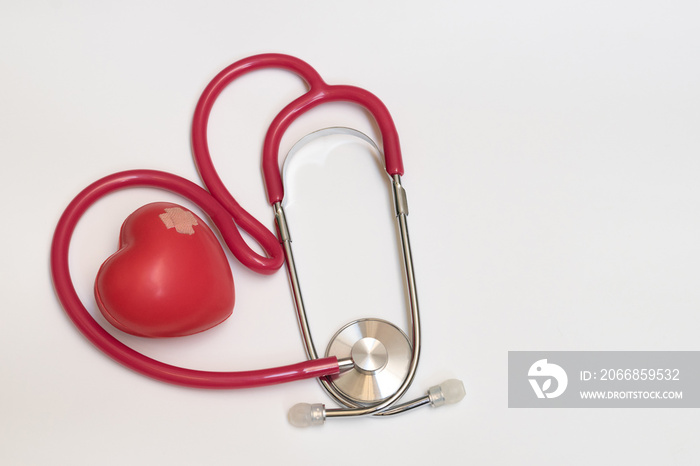 Red doctor stethoscope in heart shape and stress ball in heart shape with plaster on as having heart attack illness being cure isolated on white background. Medical healthcare concept.