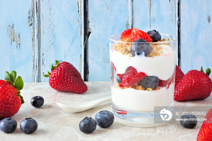 Strawberry and blueberry parfait in a glass against a rustic blue wood background