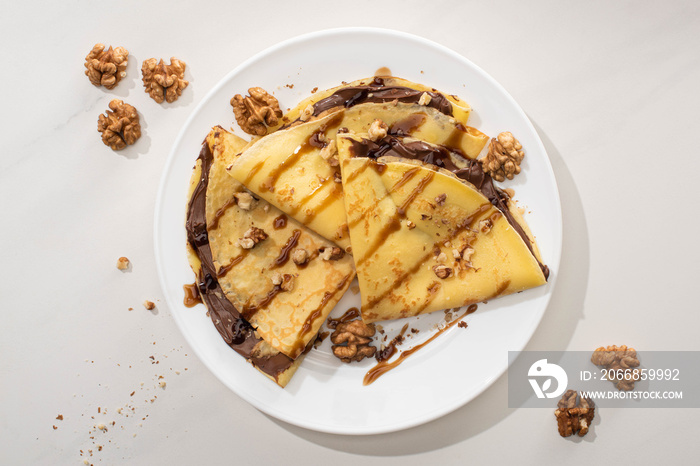 top view of tasty crepes with chocolate spread and walnuts on plate on grey background