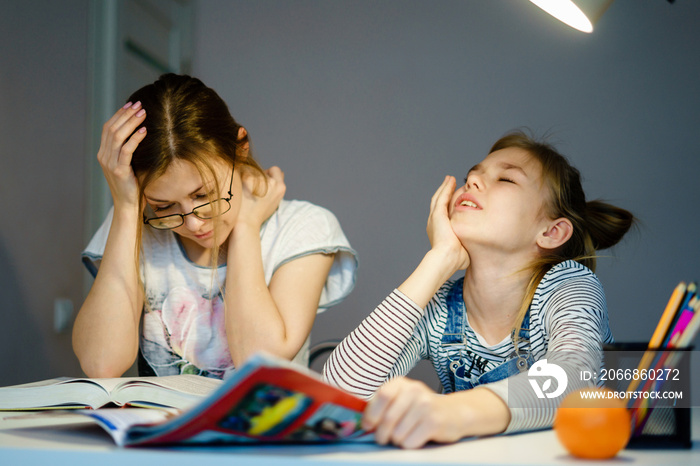 Mother helping her tired daughter with homework at home.