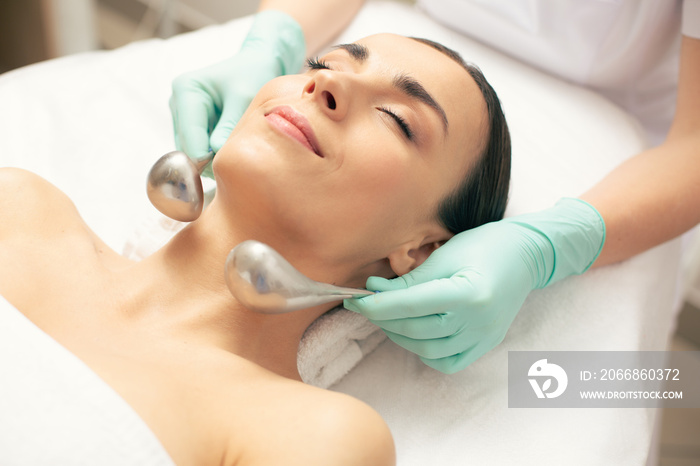 Hands of beautician holding cryo-sticks near the face of woman