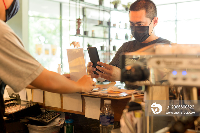 Male customer with protective mask paying bill by cell phone in cafe.