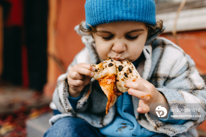 Closeup of a little boy eating a slice of pizza outdoors.