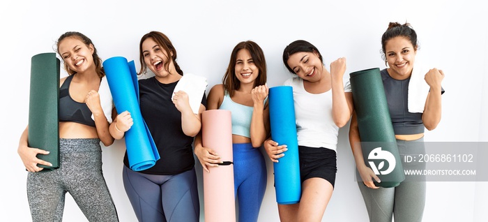 Group of women holding yoga mat standing over isolated background very happy and excited doing winner gesture with arms raised, smiling and screaming for success. celebration concept.