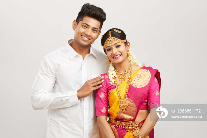 Attractive happy south Indian couple in traditional dress on white.