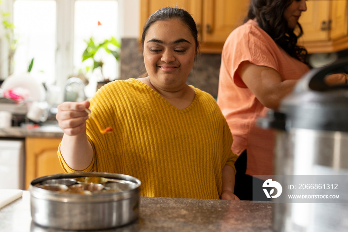 Woman with down syndrome adding spices while cooking with mother in kitchen