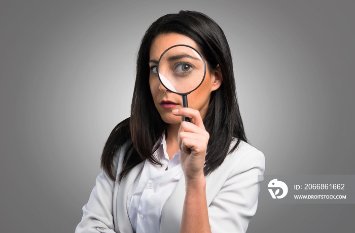 Pretty woman with magnifying glass on grey background