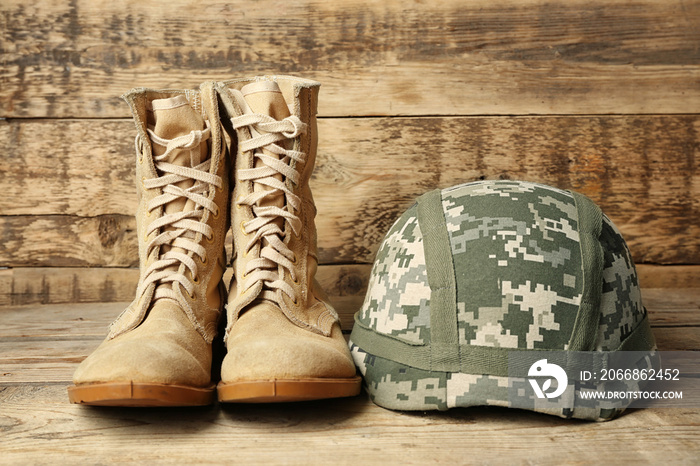 Pair of combat boots and military helmet on wooden background, close up