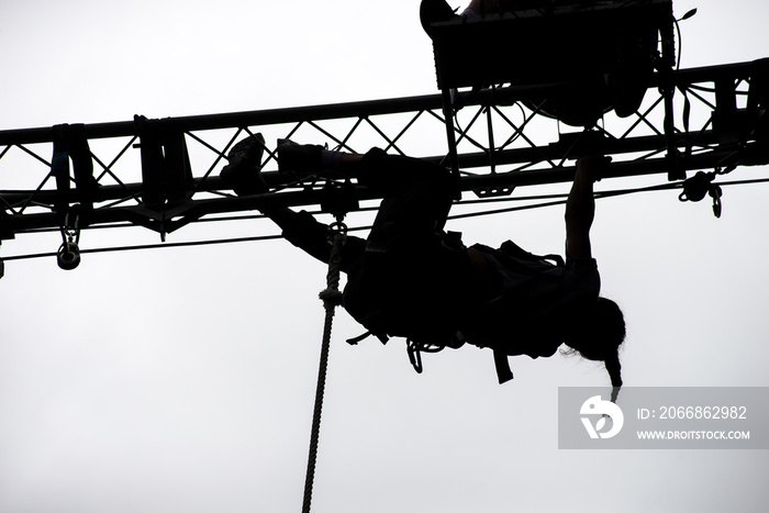 Silhouette of girl climbing on metallic structure on cloudy sky background