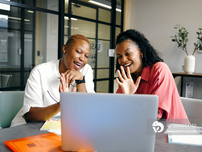 Two women waving at laptop in office