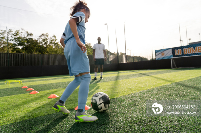 Coach watching girl (6-7) practicing on soccer field