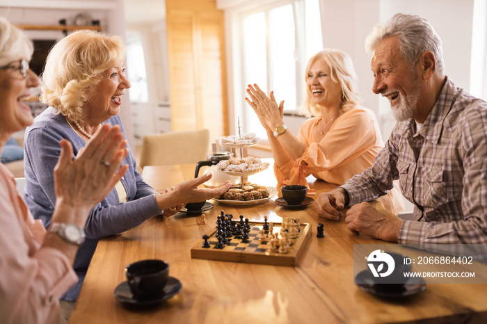 Happy seniors communicating while playing chees at home.