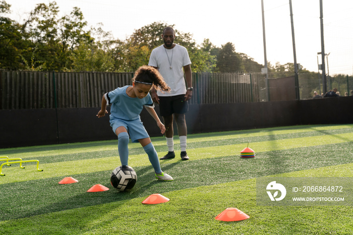 Coach watching girl (6-7) practicing on soccer field