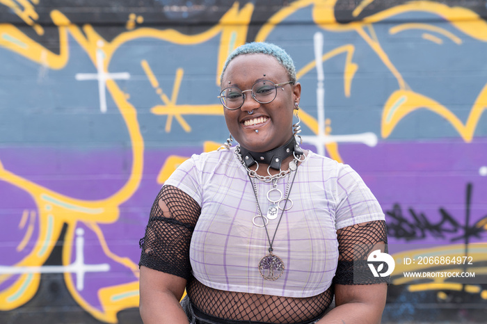 Portrait of smiling non-binary person against graffiti wall