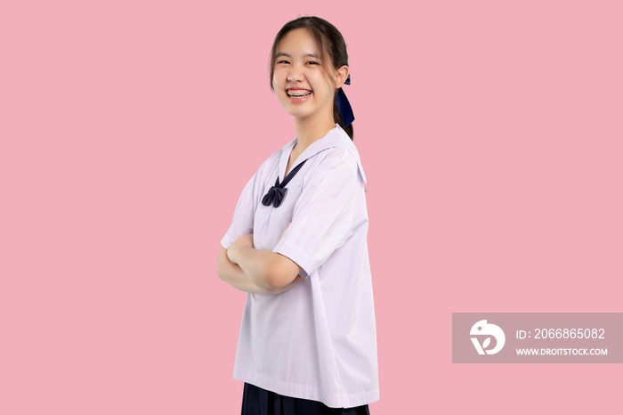 Happy braces Asian student girl in school uniform arm crossed on isolated pastel background.