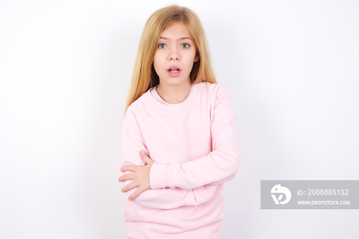 Shocked embarrassed Beautiful caucasian blonde little girl wearing pink sweater keeps mouth widely opened. Hears unbelievable novelty stares in stupor