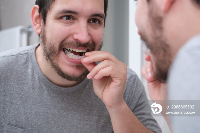 Young latin man wearing orthodontic silicone trainer or invisible braces aligner. Mobile orthodontic appliance for dental correction.