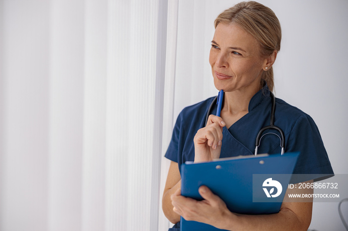 Professional woman doctor standing with clipboard and looking away in medicine center