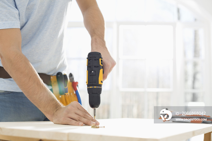 Midsection of man drilling nail on table