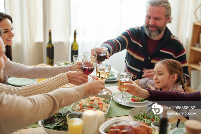 Family of six sitting by served table and clinking with drinks over festive food