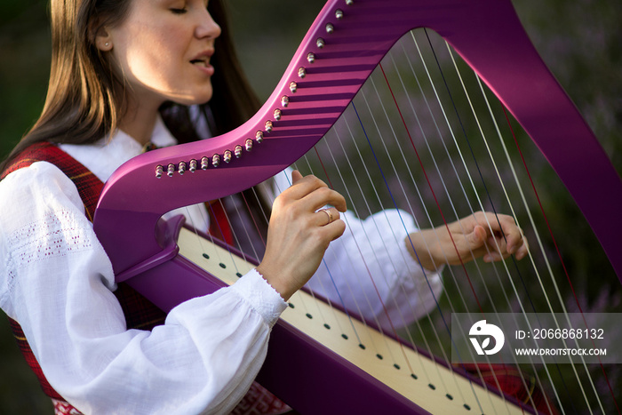 Beautiful young woman playing celtic harp and singing song in woodland