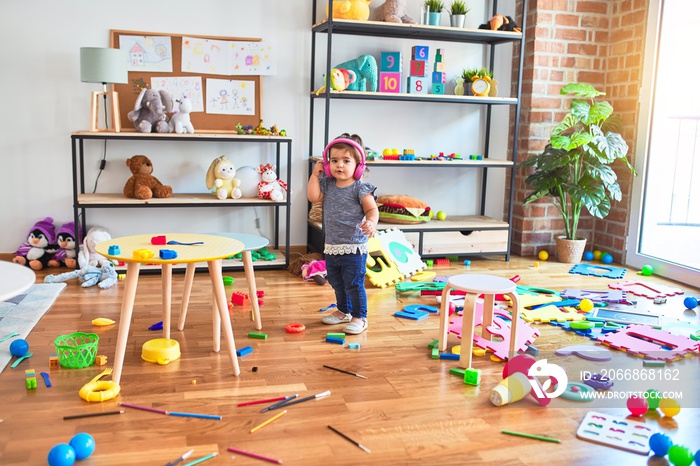 Beautiful toddler listening to music using headphones standing at kindergarten