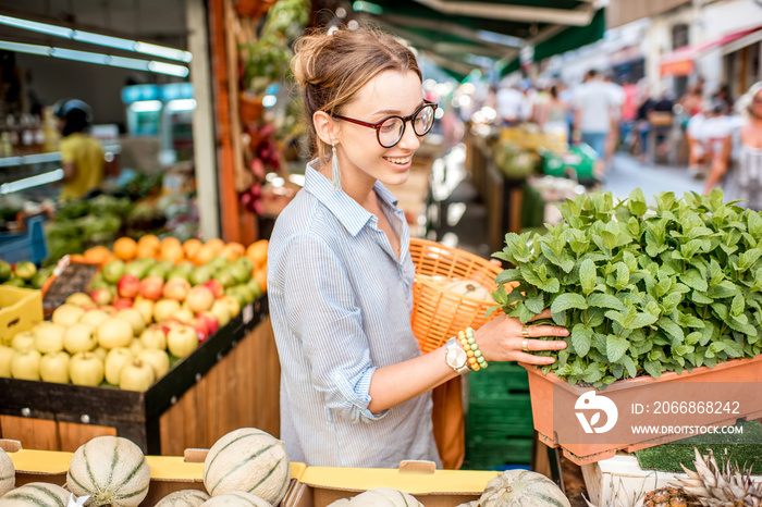 Young woman choosing a fresh mint standing with basket at the food market in France