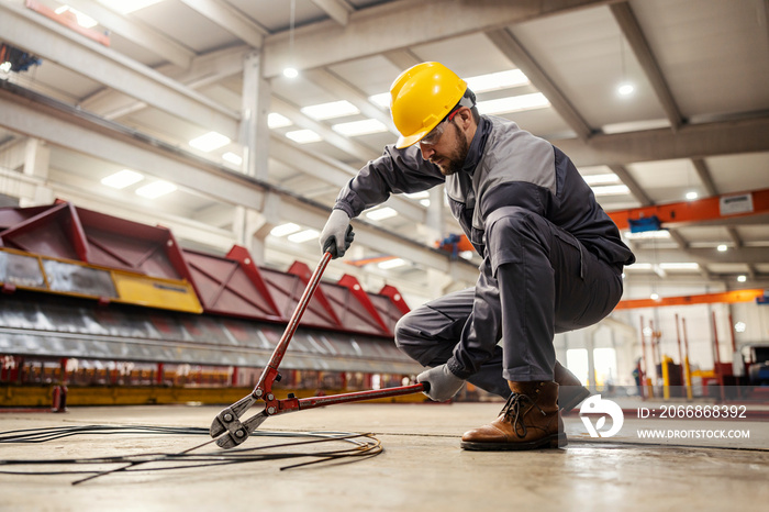 A metallurgy worker in a protective uniform uses big pliers to cut metal wires in the facility.