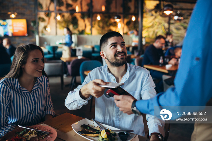 couple in restaurant. man paying contactless with smartphone