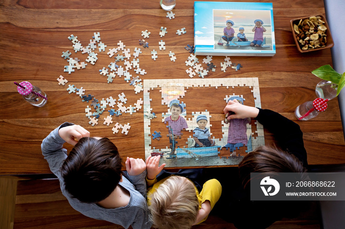 Three children, boys, assembling puzzle with their picture from the beach, playing at home