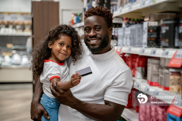 African american man holding his kid, the girl holding a credit card and smiling