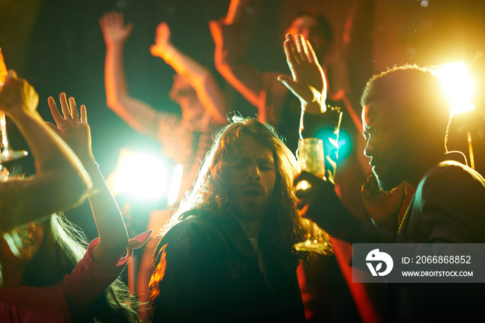 Passionate handsome young guy with long hair singing song and dancing in projector lights at party in nightclub