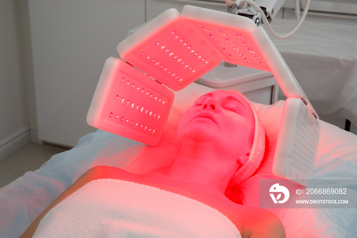 An elderly woman undergoes a facial rejuvenation procedure. Woman face lt Red light treatment At beauty clinic. Cosmetology.