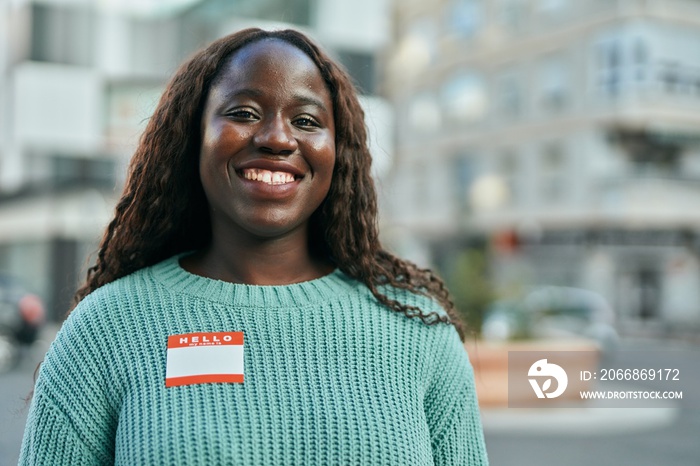 Young african woman smiling happy wearing hello i am sticker at the city