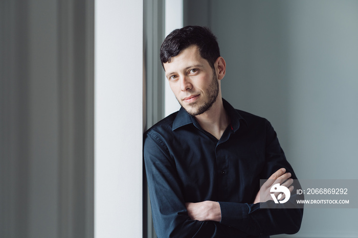 Caucasian young man portrait holding arms crossed, wearing black shirt on light background