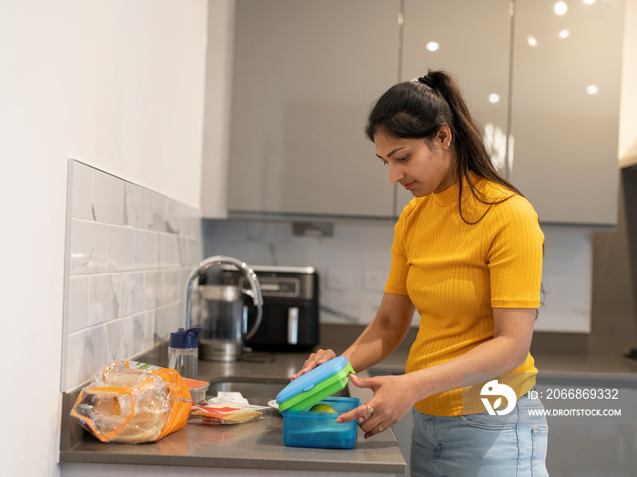 Young woman preparing lunch boxes in kitchen