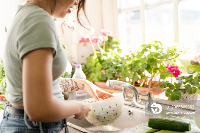 Young woman washing food in kitchen sink