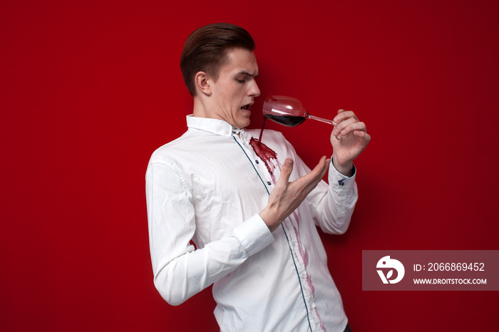 sad guy in a white shirt spilled red wine on himself on a red background, an angry man put a stain of wine on his clothes