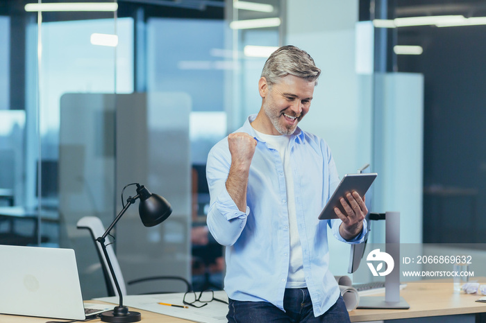 Senior and experienced business man uses a tablet to work, gesture of victory hand, received good news