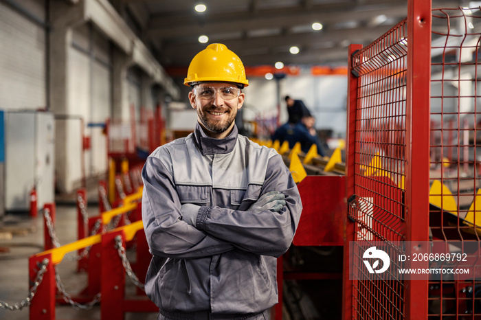 A heavy industry worker stands in a facility with arms crossed and smiling at the camera.