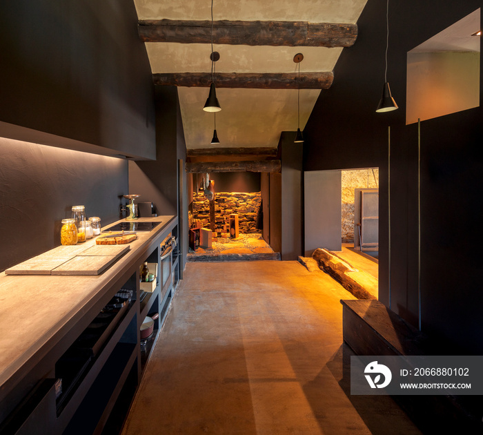 Modern kitchen front view in a renovated mountain chalet. At the back there is the pantry with hanging salami and ham and some bottles of wine