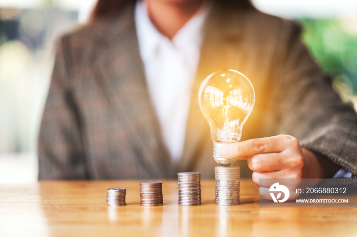 Businesswoman holding and putting light bulb on coins stack on the table for saving energy and money concept