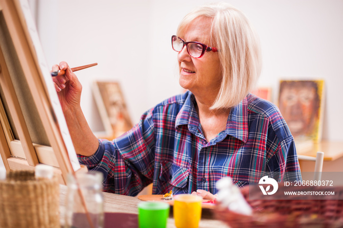 Elderly woman is painting in her home. Retirement hobby.