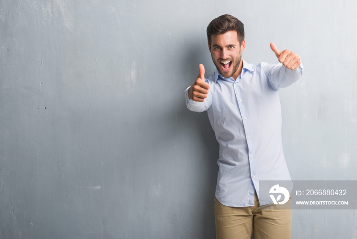 Handsome young business man over grey grunge wall wearing elegant shirt approving doing positive gesture with hand, thumbs up smiling and happy for success. Looking at the camera, winner gesture.