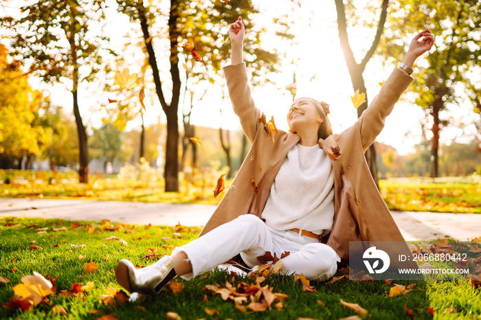 Young woman in park on sunny autumn day, smiling, having fun with leaves. Autumn fashion. Lifestyle. Relax, nature concept.