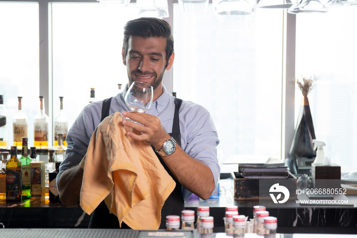 Young caucasian man is bartender cleaning and wipe glass with professional at counter, portrait handsome male preparation glass or wineglass, barman standing with confident at restaurant luxury.