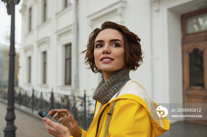 Woman in yellow raincoat with smartphone in hand